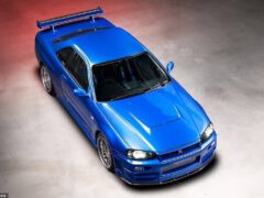 Een bovenaanzicht van een blauwe sportwagen met een achterspoiler en een gedetailleerde grille aan de voorkant, die doet denken aan de Fast & Furious-serie, binnenshuis geparkeerd op een betonnen ondergrond.