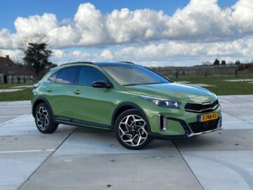 Een groene Kia XCeed crossover-SUV staat geparkeerd op een betonnen terrein met een landelijk landschap en bewolkte lucht op de achtergrond.