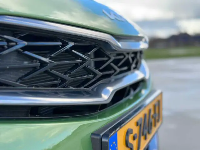 Close-up van de grille en de Europese kentekenplaat van een groene Kia XCeed, met een wazige buitenomgeving op de achtergrond.