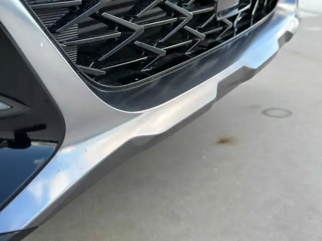 Close-up van een Kia XCeed-voorbumper met een zilver-, zwart- en glanzend grijs kleurenschema, met de onderste grille en een deel van de voorlip.