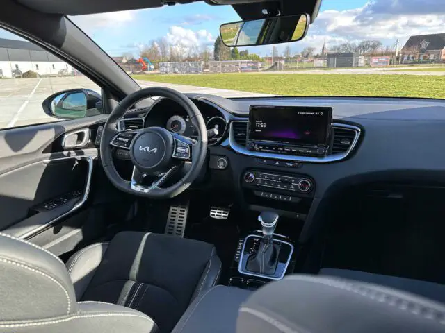 Binnenaanzicht van een moderne Kia XCeed, met de nadruk op de bestuurdersstoel, het stuur met Kia-logo, centraal dashboard met touchscreendisplay, versnellingspook en diverse bedieningsknoppen.