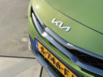 Close-up van de voorkant van een groene Kia XCeed-auto met de focus op het Kia-logo en een gedeeltelijke weergave van de gele kentekenplaat beginnend met 9-1.