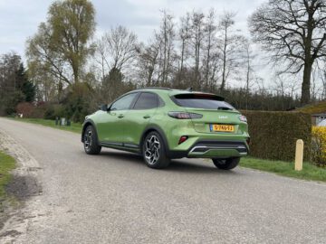 Een groene Kia XCeed staat geparkeerd op een landelijke weg met bomen en struiken op de achtergrond, onder een bewolkte hemel, en laat zijn elegante ontwerp zien tegen de schilderachtige achtergrond van de natuur.