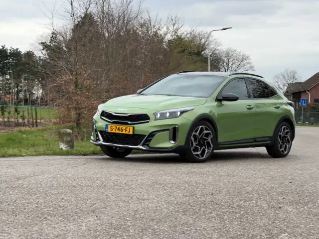 Een groene Kia XCeed-crossover met kenteken S-746-FJ staat op een bewolkte dag geparkeerd op een verharde weg nabij enkele bomen en huizen.