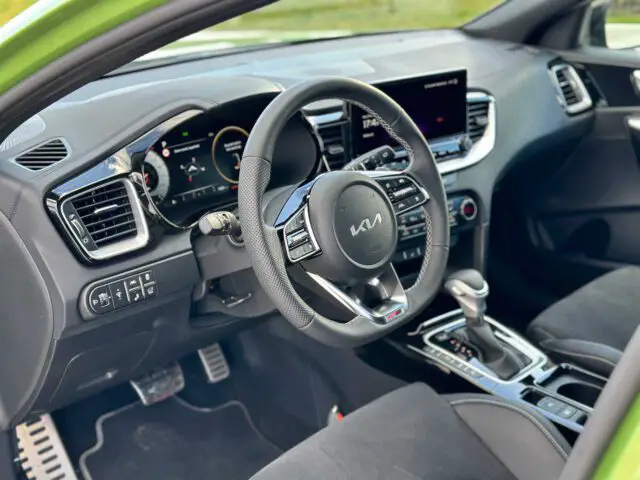 Binnenaanzicht van een moderne Kia XCeed met een zwart stuur met het Kia-logo, digitaal dashboard, touchscreendisplay, versnellingspook en verschillende bedieningselementen op de middenconsole en het stuur.