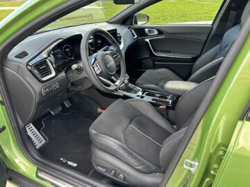 Binnenaanzicht van een groene Kia XCeed met zwart beklede stoelen, een modern dashboard met digitaal display, een stuur met bedieningselementen en een versnellingspook in de middenconsole.