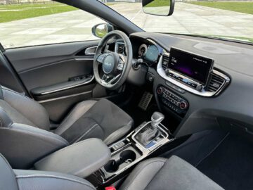 Binnenaanzicht van een moderne Kia XCeed met het stuur, het dashboard, het touchscreen, de versnellingspook en de voorstoelen. Het interieur is voorzien van zwarte bekleding en metallic accenten.