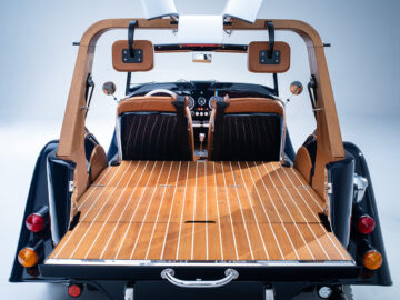 Achteraanzicht van een op maat gemaakt Morgan Plus 4 Spiaggina-auto-interieur met houten vloeren, lederen stoelen en openslaande vleugeldeuren. Op de achtergrond zijn het dashboard en het stuur zichtbaar.