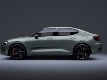 Zijaanzicht van een strakke, matgroene Polestar 2 BST edition 230 sedan met zwarte velgen en getinte ruiten, tegen een effen donkere achtergrond.