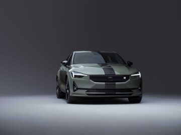 Een groene Polestar 2 BST editie 230 elektrische auto met zwarte racestrepen, tentoongesteld tegen een grijze achtergrond, vooraanzicht.