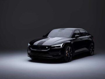 Een strakke zwarte Polestar 2 BST edition 230 elektrische sedan wordt tentoongesteld tegen een donkere achtergrond in een studioomgeving, wat het moderne design en de koplampen benadrukt.