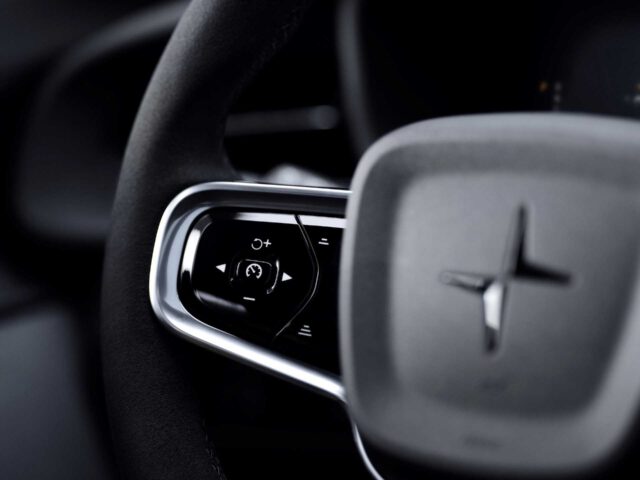 Close-up van een autostuur met geïntegreerde bedieningsknoppen, met een strak, modern ontwerp en het prominente Polestar 2 BST edition 230-logo in het midden.