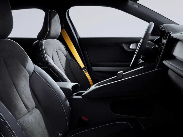 Interieur van de Polestar 2 BST Edition 230 met zwarte stoffen stoelen, een gele veiligheidsgordel en een strak dashboardontwerp. Het stuur en de middenconsole zijn zichtbaar.