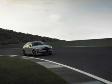 Een Polestar 2 BST edition 230 met donkere accenten rijdt op een gebogen baan omgeven door groene heuvels onder een bewolkte hemel.