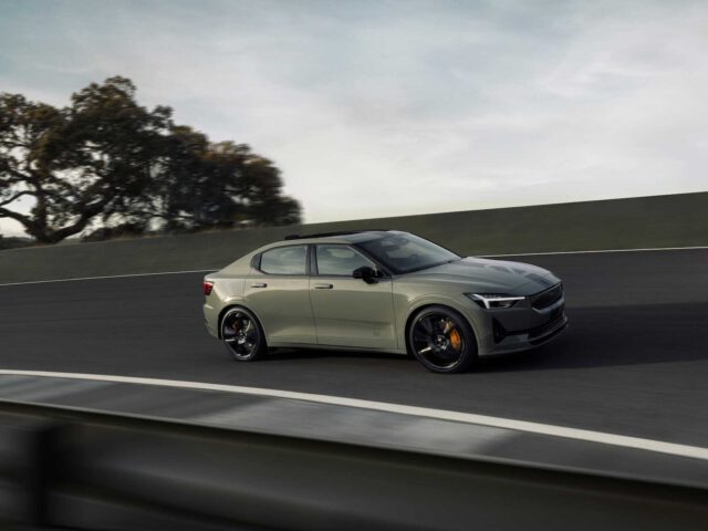 Een Polestar 2 BST edition 230, met zijn strakke beige design en donker getinte ramen, navigeert over een bochtige weg omzoomd met bomen onder een bewolkte hemel.