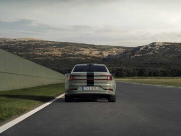 Een Polestar 2 BST Edition 230 met een zwarte racestreep zoeft over het circuit, met op het kenteken "MLB 808". Op de achtergrond voegen heuvels en een bewolkte lucht drama toe aan het tafereel.