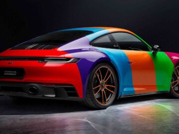 Binnen staat een felgekleurde Porsche 911 Carrera GTS met regenboogkleuren geparkeerd, met een strak ontwerp aan de achterkant, grote wielen en een verlichte omgeving.