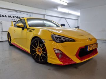 Een gele Toyota GT86 met zwarte en rode details staat in een garage onder fel licht. Op het kenteken staat "SV-248-T.