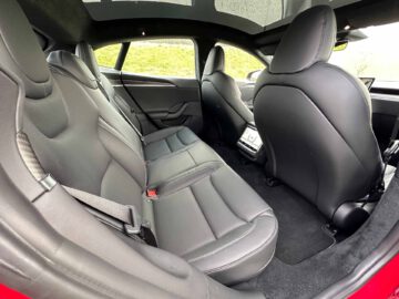 Binnenaanzicht van een Tesla Model S Plaid met zwartleren stoelen, een ruime zithoek achterin en een middenconsole met een klein scherm.