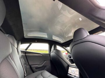 Het luxueuze interieur van een Tesla Model S Plaid is voorzien van zwart lederen stoelen, een touchscreen op de achterbank en een groot panoramisch zonnedak. De hoek loopt van de achterbank en kijkt naar voren, wat het strakke en moderne ontwerp benadrukt.