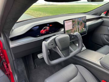 Interieur van een Tesla Model S Plaid met het stuurjuk, een digitaal dashboard met een rood autodisplay en een groot touchscreen met kaarten en routebeschrijvingen.