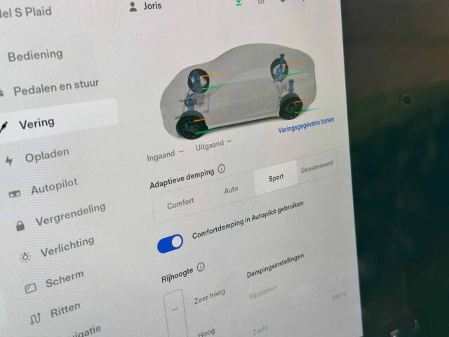 Close-up van de touchscreen-interface van een Tesla Model S Plaid met ophangingsinstellingen, inclusief opties zoals adaptieve demping, comfort, auto en sport. Beelden op het scherm tonen schokdempers op een voertuigdiagram.