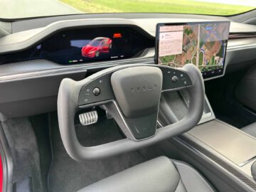 Binnenaanzicht van de Tesla Model S Plaid met een stuurwiel in jukstijl, een digitaal instrumentenpaneel met daarop een auto en een touchscreen met een kaart.