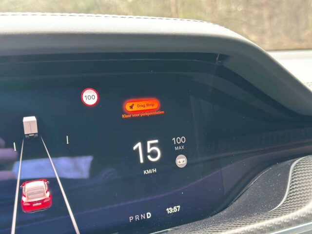 Een Tesla Model S Plaid-dashboarddisplay met een snelheid van 15 km/u met een maximumsnelheid van 100 km/u. Op het scherm staat "Drag Strip Klar voor plekjehighse." De weergegeven tijd is 13:57.