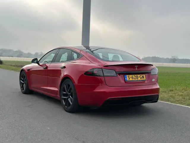 Een rode Tesla Model S Plaid geparkeerd op een weg nabij een grasveld, met een bewolkte lucht op de achtergrond. Nederlands kenteken "S-628-GN" is zichtbaar.