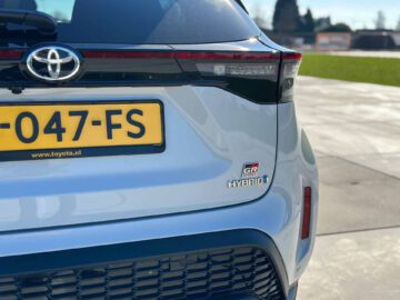 Achteraanzicht van een lichtblauwe Toyota Yaris Cross GR Sport hybride auto met de kentekenplaat, GR Sport-badge en hybride embleem.