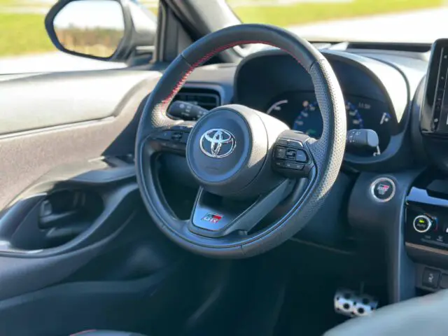 Close-up van het stuur en de bestuurdersconsole van een auto met een Toyota Yaris Cross GR Sport-logo, bedieningsknoppen en dashboarddisplay.