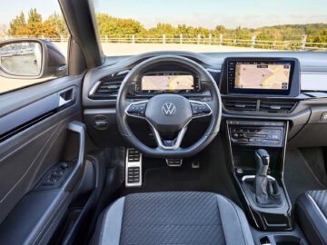 Binnenaanzicht van een moderne Volkswagen T-Roc Cabrio met het stuur met het Volkswagen-logo, het dashboard, het touchscreen-navigatiesysteem en de versnellingspook.