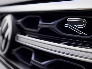 Close-up van de grille van een Volkswagen T-Roc Cabrio, met het iconische Volkswagen-logo aan de linkerkant en het kenmerkende 'R'-embleem aan de rechterkant.