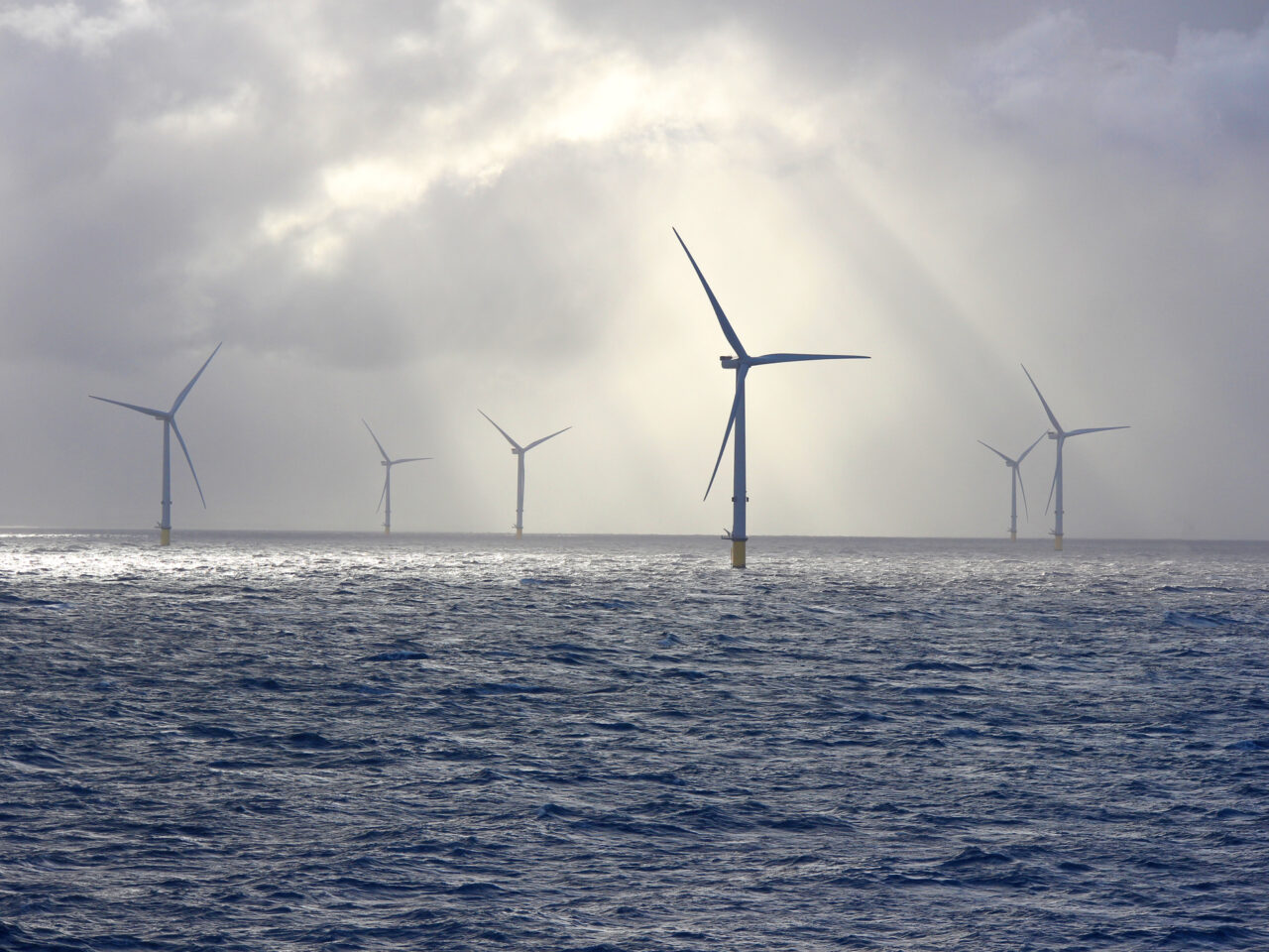 Verschillende offshore windturbines staan in de oceaan onder een bewolkte hemel waar zonlicht doorheen dringt en benutten de kracht van de natuur voor de productie van groene waterstof.