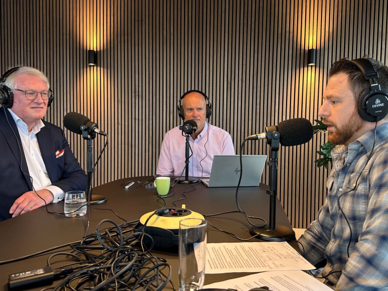 Drie mannen zitten aan een tafel met een koptelefoon op en spreken in microfoons voor de AutoRAI Podcast-opname in een studio.