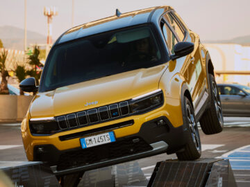 Een gele Jeep Avenger wordt gekanteld op een helling getoond, wat zijn offroad-capaciteiten in een stedelijke omgeving demonstreert. Op de kentekenplaat aan de voorkant van het voertuig staat "GM 145 TS." Deze Jeep Avenger-recensie benadrukt zijn indrukwekkende veelzijdigheid en robuust ontwerp.