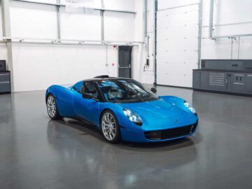 Een blauwe sportwagen met een strak aerodynamisch ontwerp staat geparkeerd in een ruime, schone en goed verlichte garage, die de verfijnde elegantie van de Gordon Murray Automotive T.33 Spider laat zien.