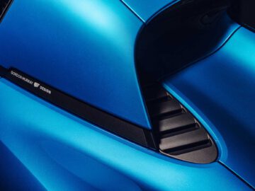 Close-up van de designdetails aan de achterkant van een blauwe Gordon Murray Automotive T.33 Spider, met de ventilatieopeningen aan de zijkant en de slanke kromming van de carrosserie.