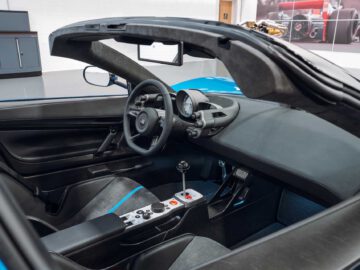 Binnenaanzicht van een Gordon Murray Automotive T.33 Spider converteerbare sportwagen met een zwart-blauw kleurenschema, met de nadruk op het stuur, het dashboard, de versnellingspook en het bedieningspaneel.