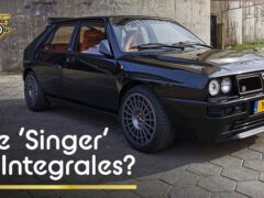 Een zwarte vintage Lancia-auto staat geparkeerd op een geplaveid terrein met 'De 'Zanger' van Integrales?' en het logo van The Late Brake Show in de afbeelding. De auto beschikt over een leesbaar kenteken met de code 