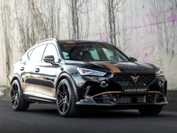 Een zwarte door Formentor gemodificeerde SUV van Manhart staat geparkeerd op een weg met een met graffiti bedekte betonnen muur op de achtergrond. De SUV is voorzien van gouden accenten en is voorzien van aftermarket wielen.