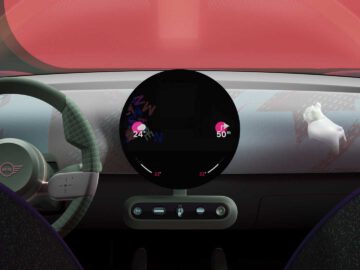 Een modern autodashboard met een rond centraal display met 24 en 50 iconen, een stuur met het MINI-logo en een kleine groene vaas met een bloem aan de rechterkant. Het strakke ontwerp integreert op subtiele wijze MINI Spike voor een verbeterde rijervaring.