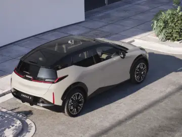 Een witte elektrische SUV, de ZEEKR X, staat geparkeerd in een geplaveide straat vlakbij de hoek van een gebouw, met groen zichtbaar op de achtergrond. Het voertuig heeft een panoramisch glazen dak en een modern design.