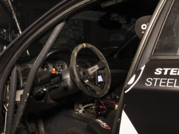 Interieur van een BMW 130i Challenge-raceauto met een stuur, dashboard met meters, rolkooi en bestuurdersstoel met veiligheidsharnas.