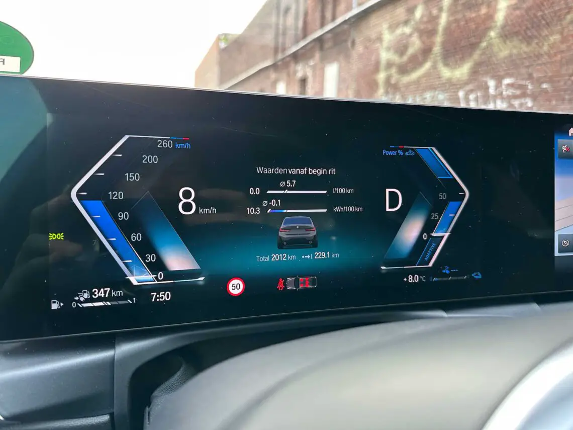 Het dashboarddisplay van de BMW 320e toont rijgegevens: snelheid van 8 km/u, versnelling in 'D', totale afstand van 2012 km, gegevens over het brandstofverbruik en een totale actieradius van 347 km. De tijd is 7.50 uur en de temperatuur is 8°C.