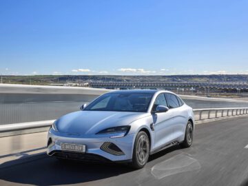 Een zilverkleurige BYD Seal sedan rijdt op een snelweg met helderblauwe luchten en een weids landschap op de achtergrond.