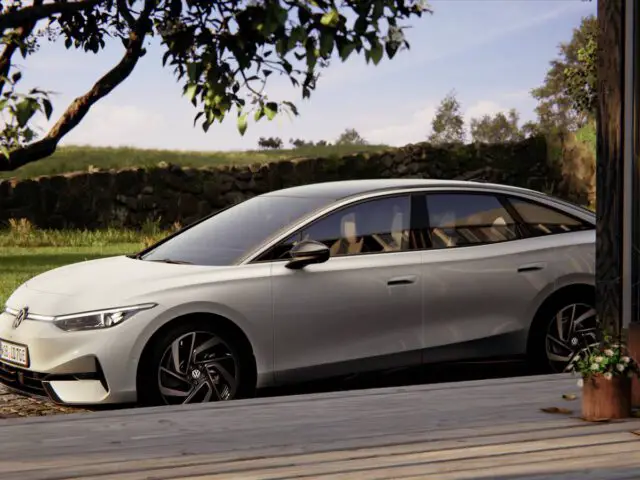 Een strakke witte elektrische sedan ID.7 staat geparkeerd in een serene buitenomgeving nabij een houten terras, omgeven door groen en struiken.