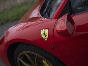 Close-up van een rode Ferrari 458 Italia-sportwagen, met het gele steigerende paardembleem op het spatbord en een zijspiegel.