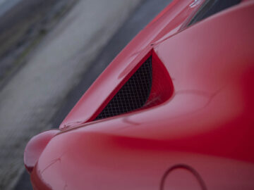 Close-up van de luchtinlaat van een rode sportwagen van Ferrari 458 Italia en aerodynamische ontwerpdetails op een onscherpe buitenachtergrond.