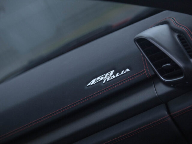 Close-up van een Ferrari 458 Italia-dashboard met rood stiksel, met het logo "458 Italia" en een ventilatieopening aan de rechterkant.